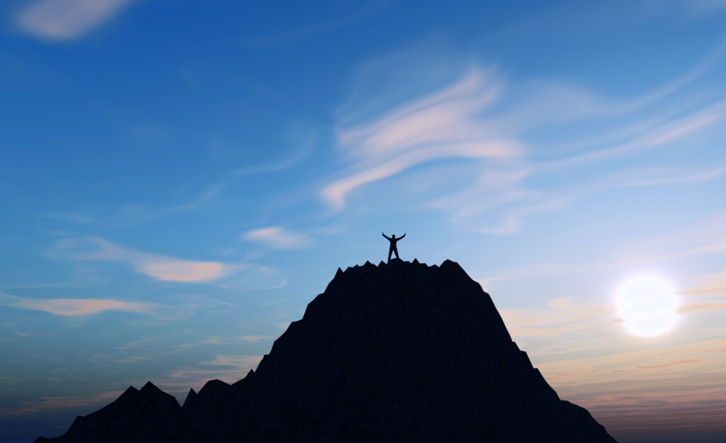 3D male figure on top of a mountain holding his arms up in succe